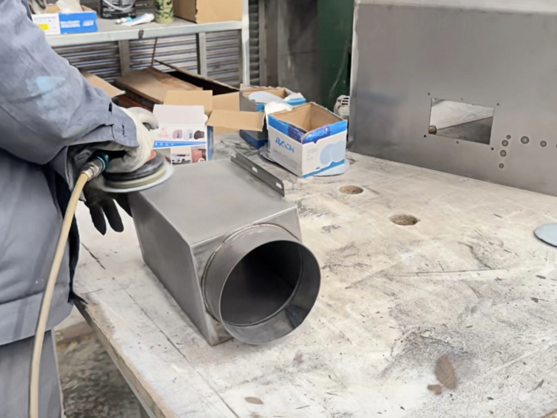 Worker finishing a fabricated metal housing with a circular duct opening