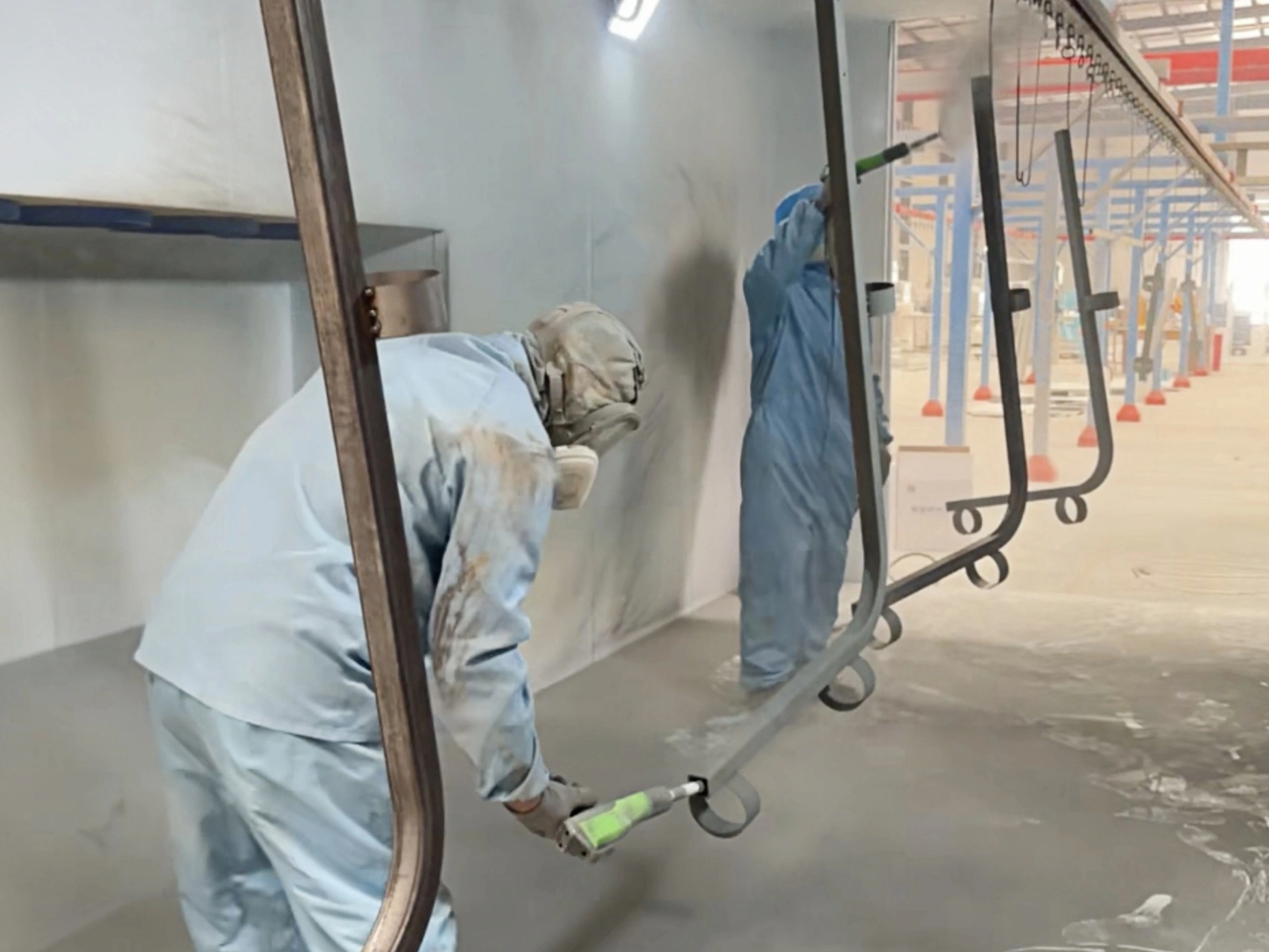 Worker spray-coating suspended metal components inside a workshop coating booth