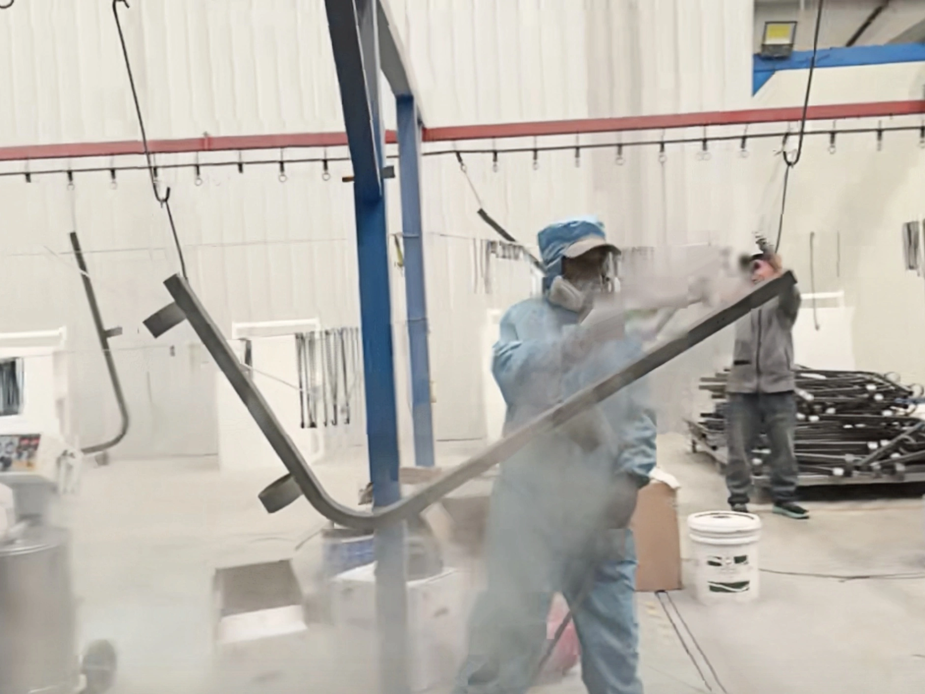Worker applying a coating to a suspended metal frame in the workshop